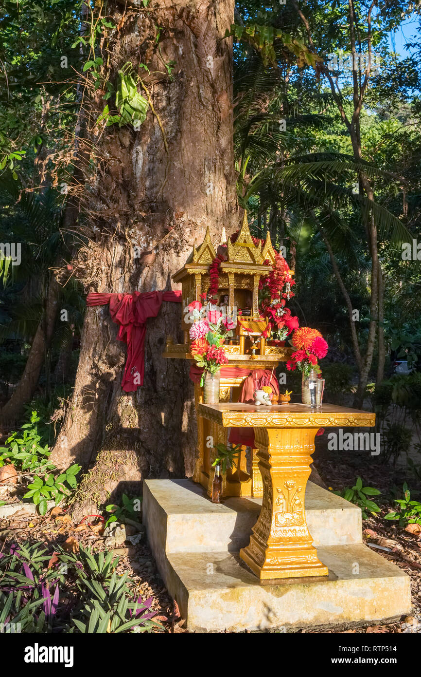 Spirit house en Thaïlande avec des guirlandes de fleurs près du grand arbre Banque D'Images