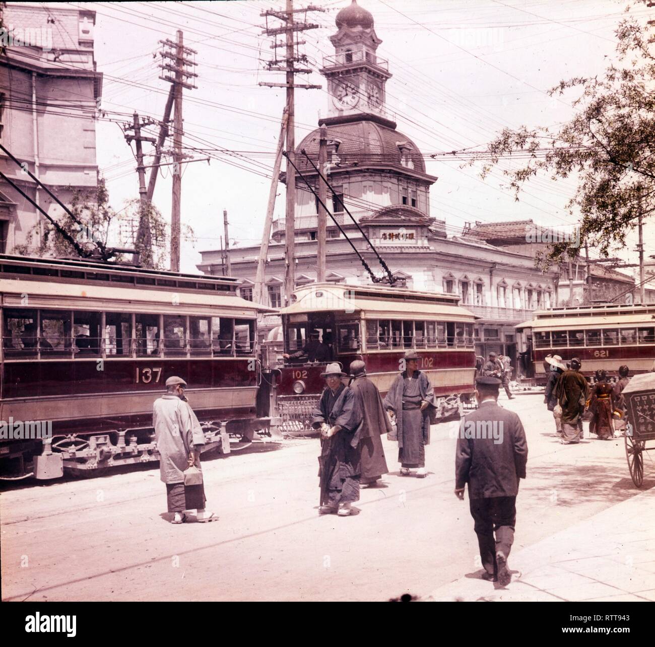 Photo colorisée des piétons et des tramways sur Ginza Crossing avec le bâtiment Hattori et le clocher de l'autre côté de la rue, Tokyo, Japon, vers le début des années 1920. (Photo de Burton Holmes) Banque D'Images