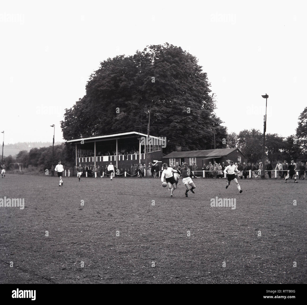 1967, match de football amateur à Tring Town FC, Tring, Herts, England, UK montrant joueurs sur le terrain, les spectateurs et les petits bois tribune et snack-hut. Pour la saison 1967-1968, le club ont été les champions de la Ligue spartiate. Banque D'Images