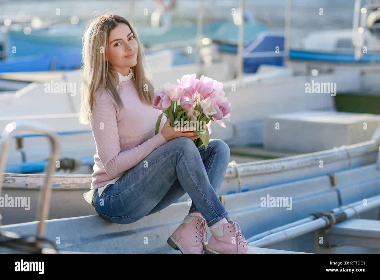 Belle jeune fille au printemps ou en automne, par la mer dans la baie en bateau. Avec un bouquet de fleurs dans ses mains et serré jeans élégant et un chandail rose Banque D'Images