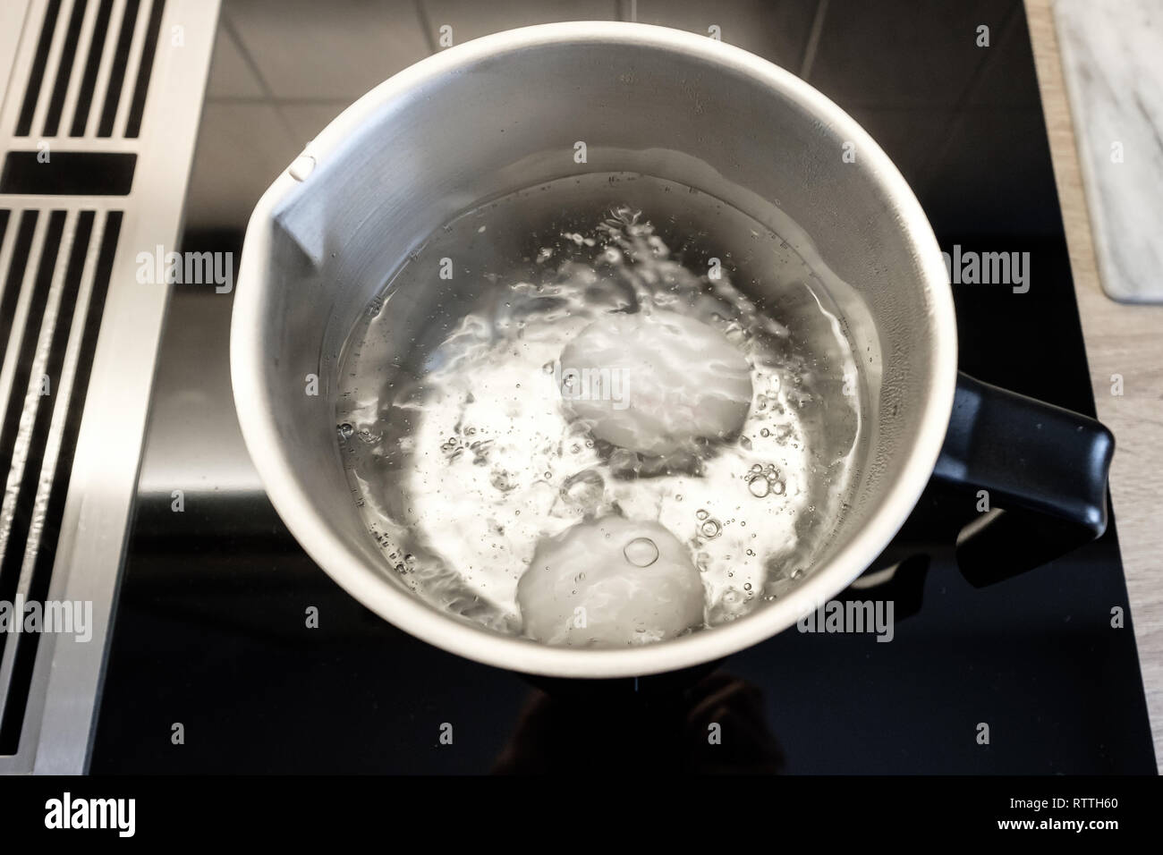 Faire bouillir les oeufs dans une casserole en acier inoxydable sur une cuisinière avec extracteur à vapeur Banque D'Images