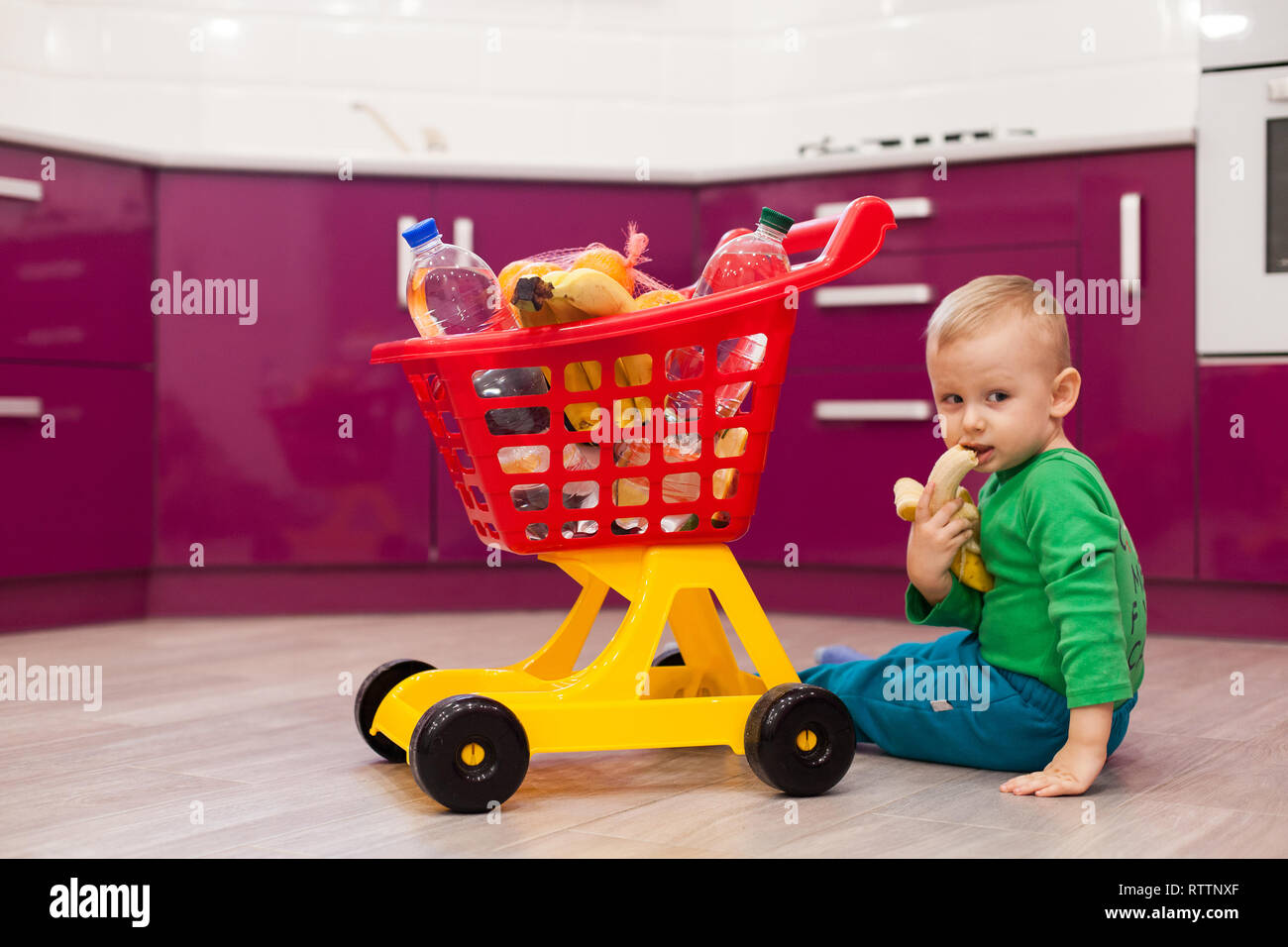 Petit garçon mange une banane. Joyeux petit garçon avec panier. Petit enfant dans la réalisation de vêtements enfant panier en plastique. Banque D'Images