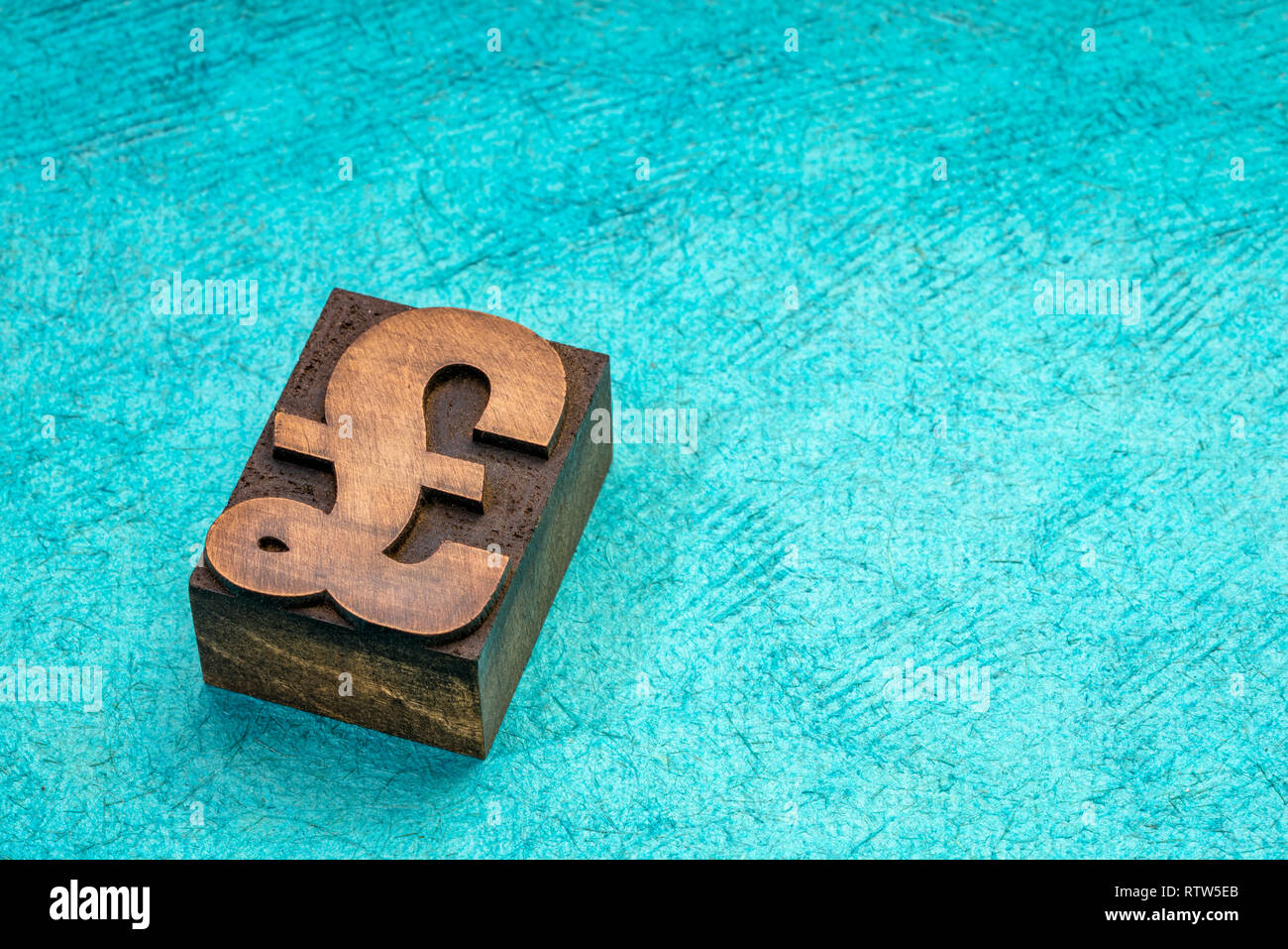 La livre sterling du symbole dans la typographie type de bloc d'impression turquoise contre du papier fait à la main avec une copy space Banque D'Images