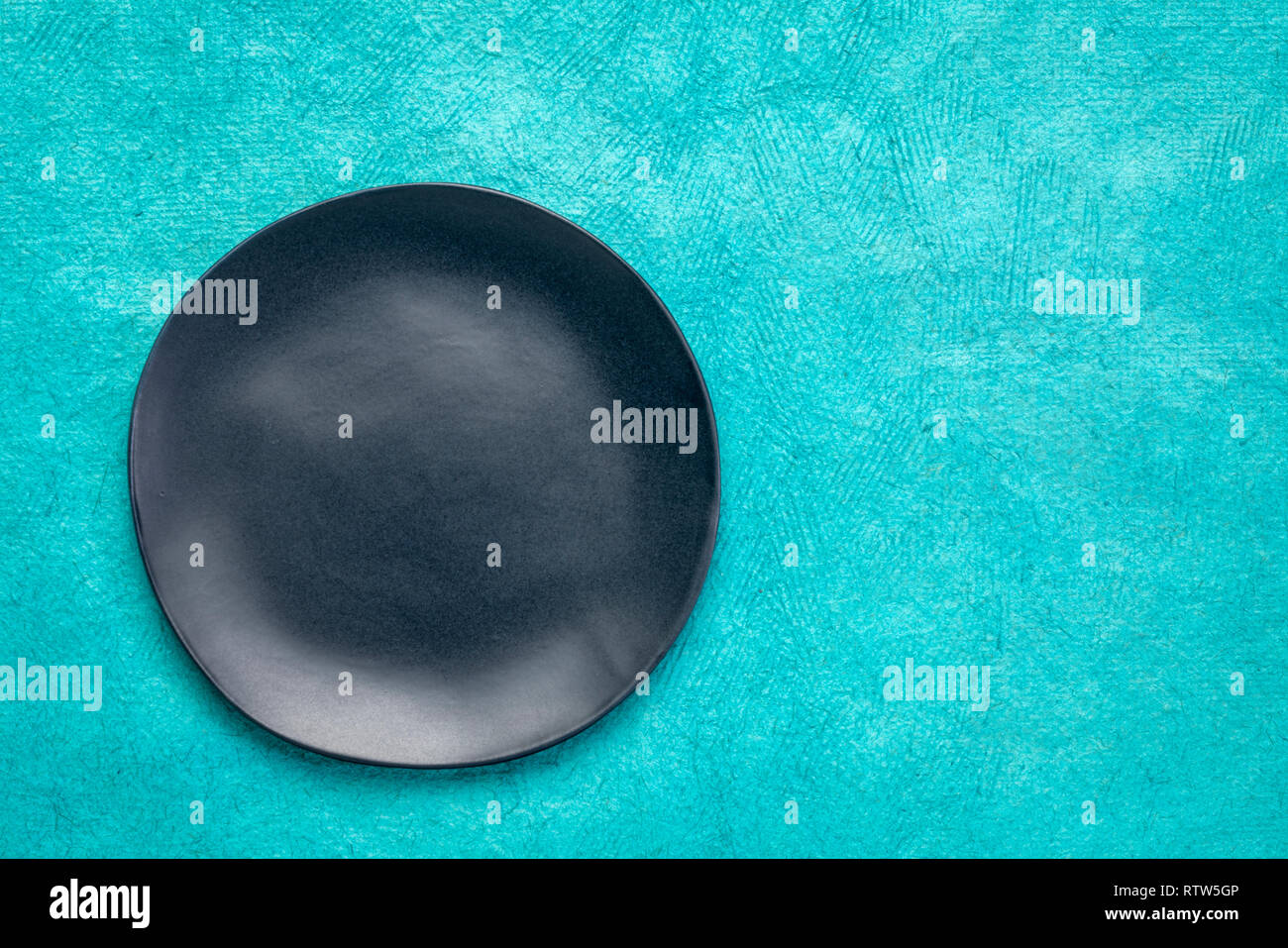 Plaque en céramique noire avec un bord irrégulier sur un papier fait main Maya Huun turquoise avec un copy space Banque D'Images