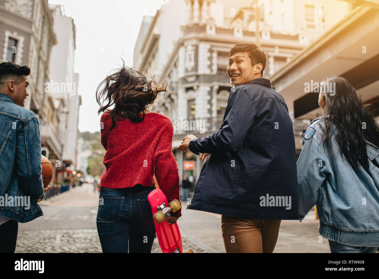 Vue arrière d'un homme asiatique souriante de se retourner tout en marchant en plein air avec des amis. Quatre jeunes gens s'amuser en plein air sur la route. Banque D'Images