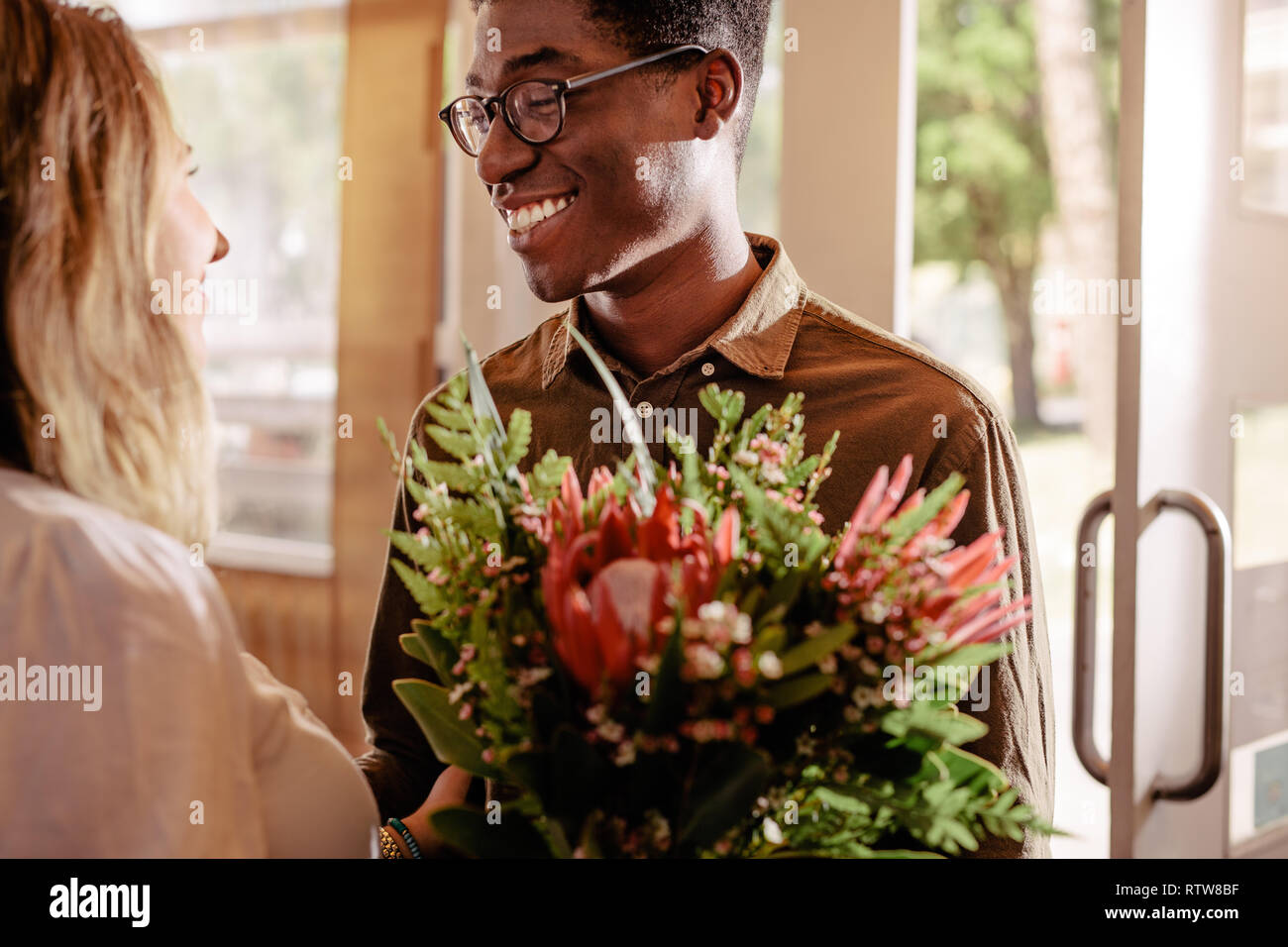 Jeune homme africain avec bouquet de fleurs rencontre sa petite amie. Homme donne des fleurs à la fille bien-aimée sur date. Banque D'Images