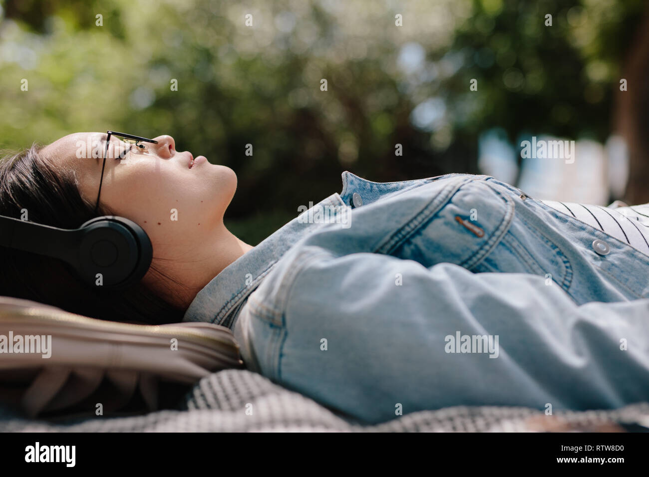 Vue latérale d'une femme de détente en plein air l'écoute de musique portant des écouteurs. Close up of a young woman sleeping en plein air dans un parc, profitant de la douceur Banque D'Images