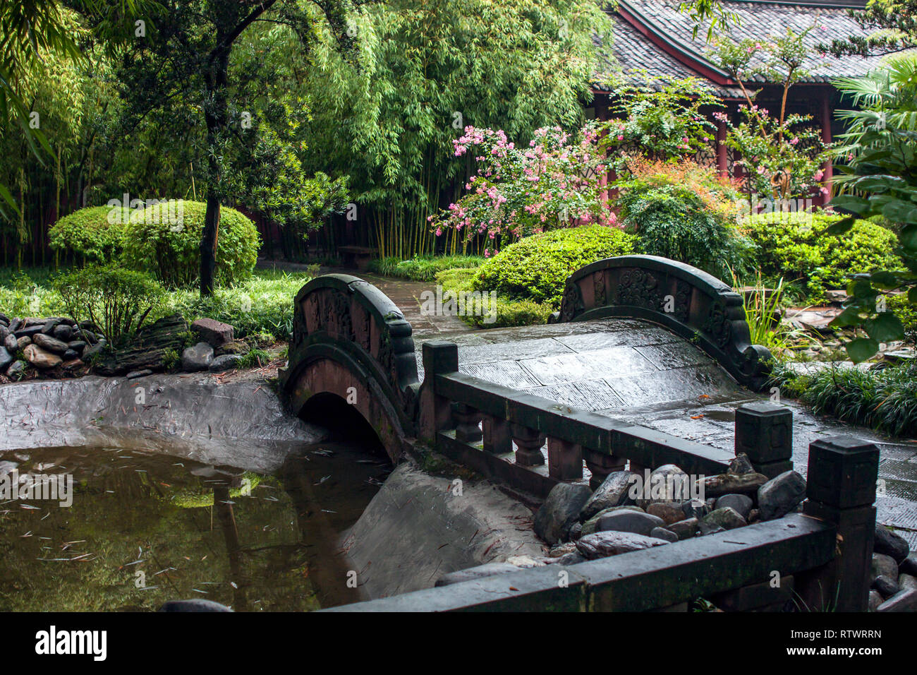 Pont de pierre dans un jardin chinois. Conception de jardin traditionnel avec pont de pierre sur un petit étang entouré d'arbres et de fleurs sur un jour de pluie. Banque D'Images