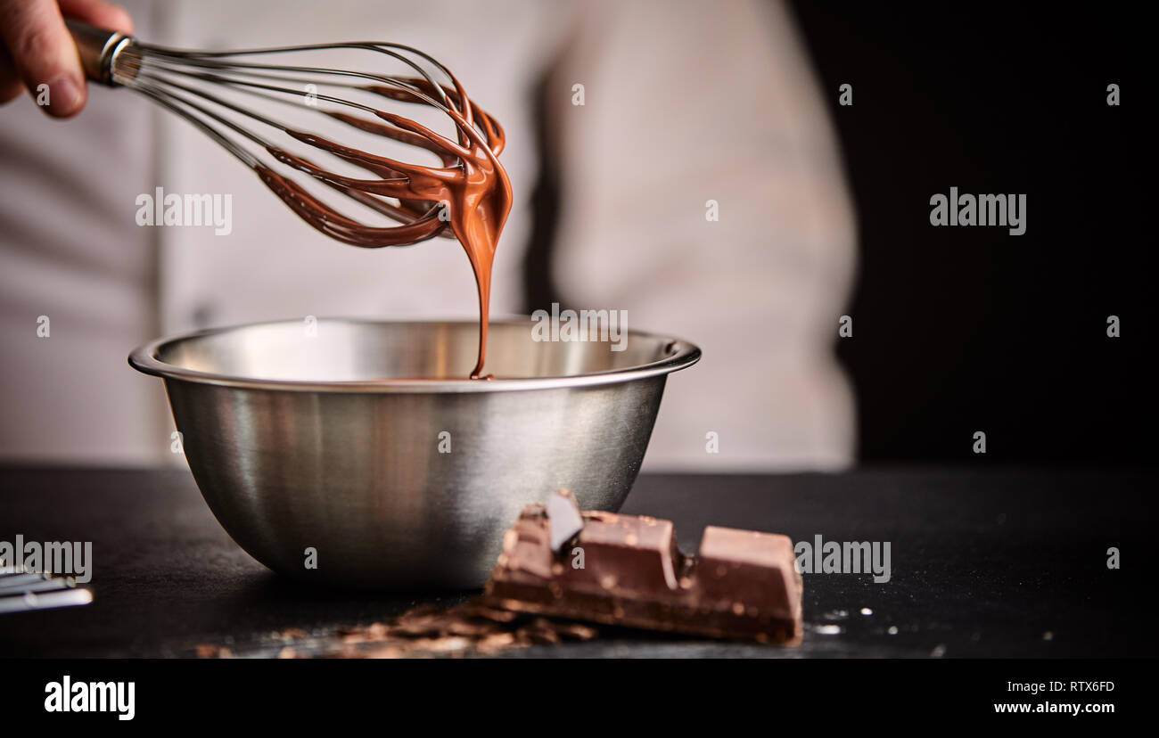 Chef boulanger ou en fouettant le chocolat fondu dans un bol avec un vieux metal fouet dans un gros plan sur sa main et ustensiles Banque D'Images