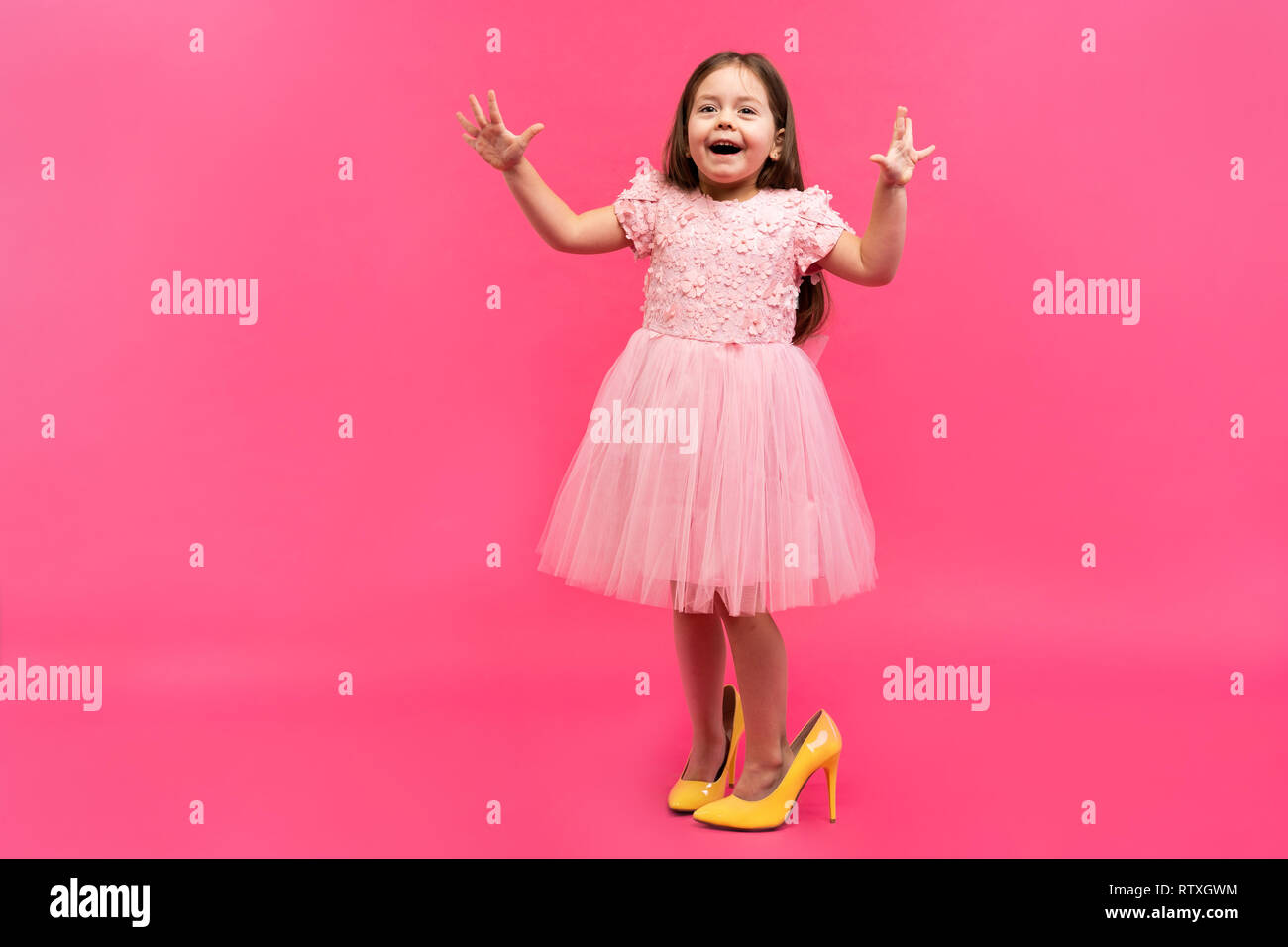 Excité incroyable happy girl in dress dans mama's shoes exprimant à la caméra isolé sur fond rose. Brightful les émotions. Banque D'Images