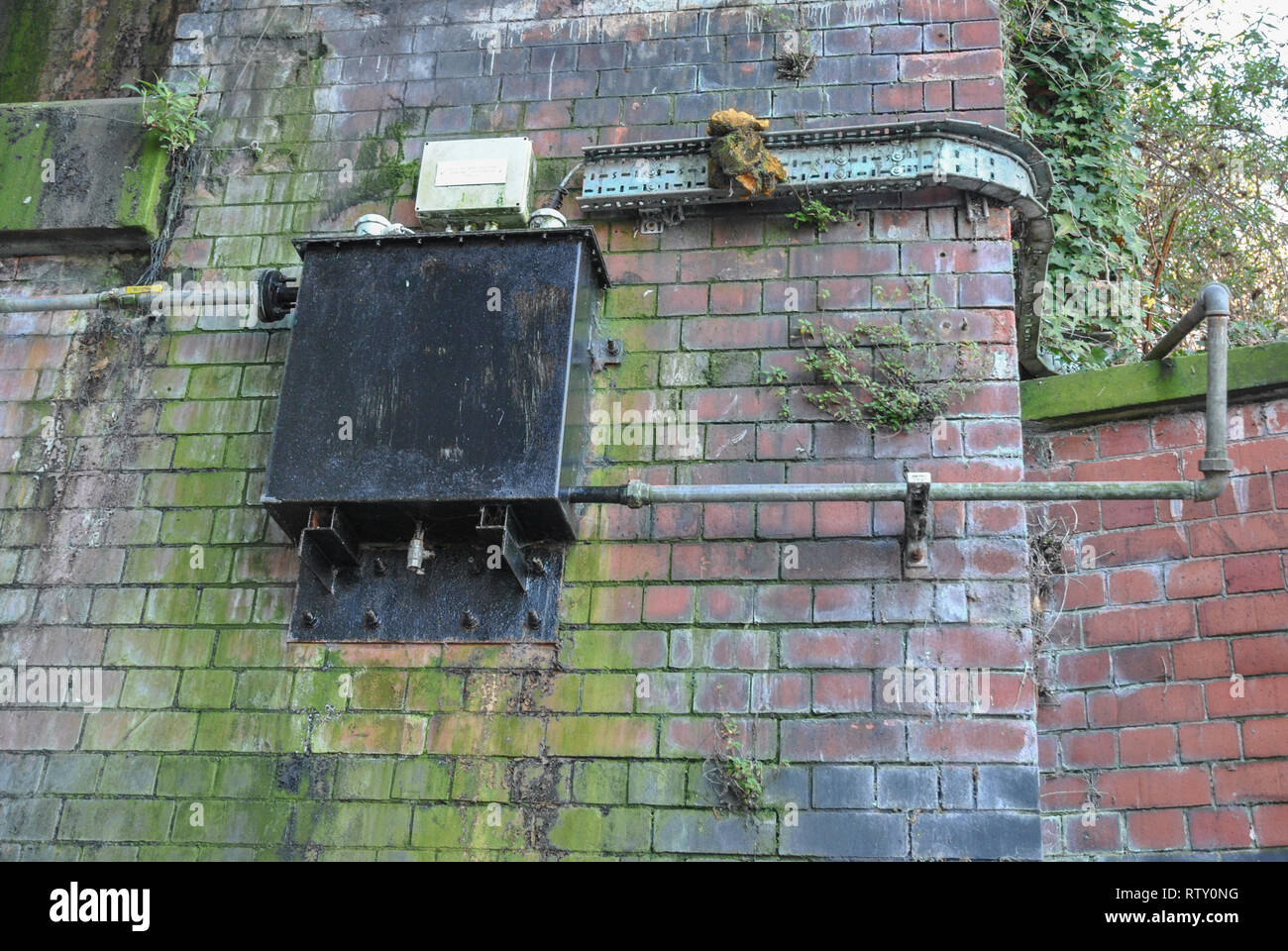 Une boîte métallique avec canalisations fixées sur un mur coloré et lichen Banque D'Images