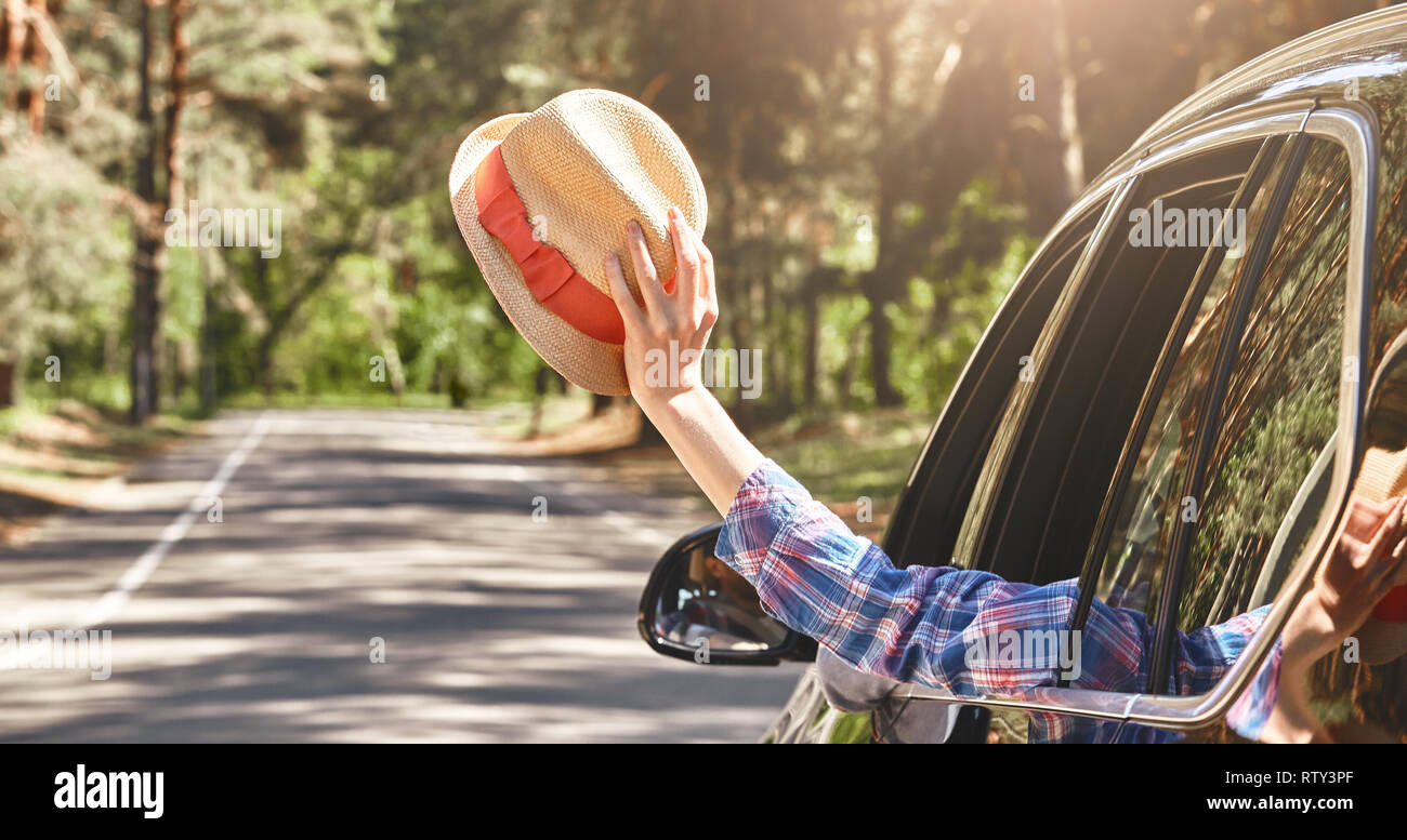 Coup de voiture brillante horizontale le long de la route. Woman waving avec un chapeau dans sa main, alors que son mari est au volant d'une voiture noire. Advenure, summertim Banque D'Images