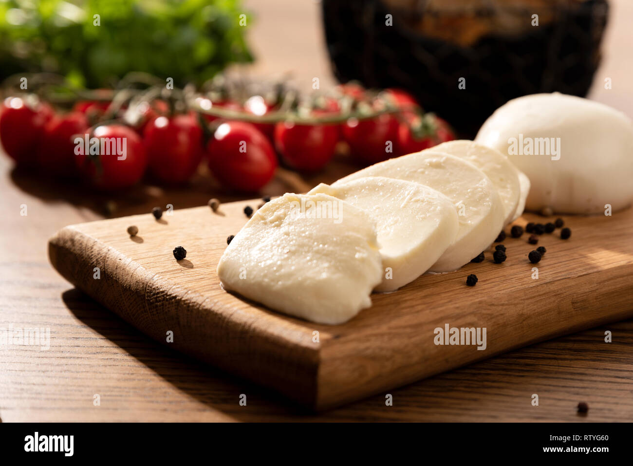 Le mozzarella sur planche en bois. Tomates cerises en arrière-plan. Table en bois avec la composition des aliments italiens Banque D'Images
