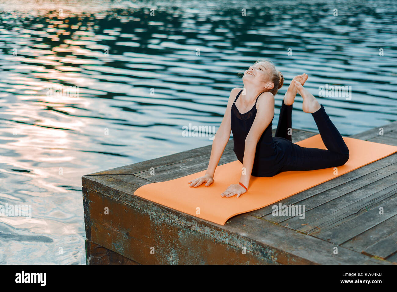 Petite fille faisant du yoga et pilates s'étendant jusqu'au bord de la rivière au coucher du soleil Banque D'Images