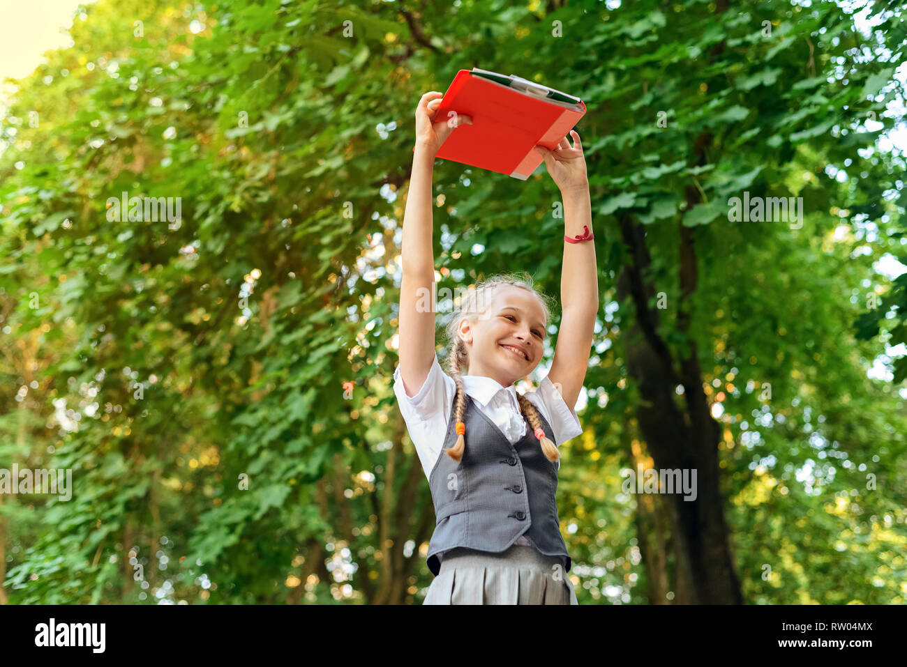 Lycéenne étudiant heureux avec des nattes en uniforme la tenue des livres dans les mains sur la tête en journée ensoleillée Banque D'Images