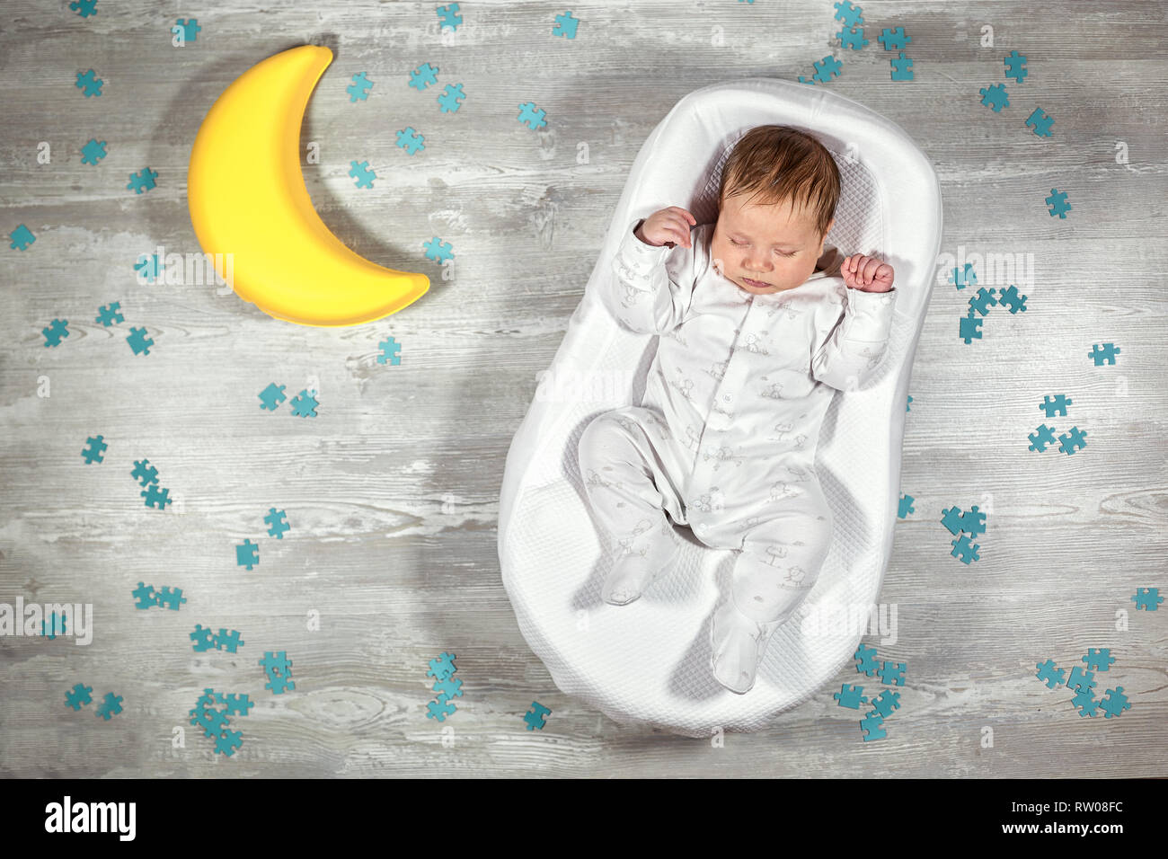 Bébé nouveau-né dort dans un matelas orthopédique spécial Baby cocoon, sur  un sol en bois, de jouets et casse-tête autour de la lune. Calme et bon  sommeil chez les nouveau-nés Photo Stock -