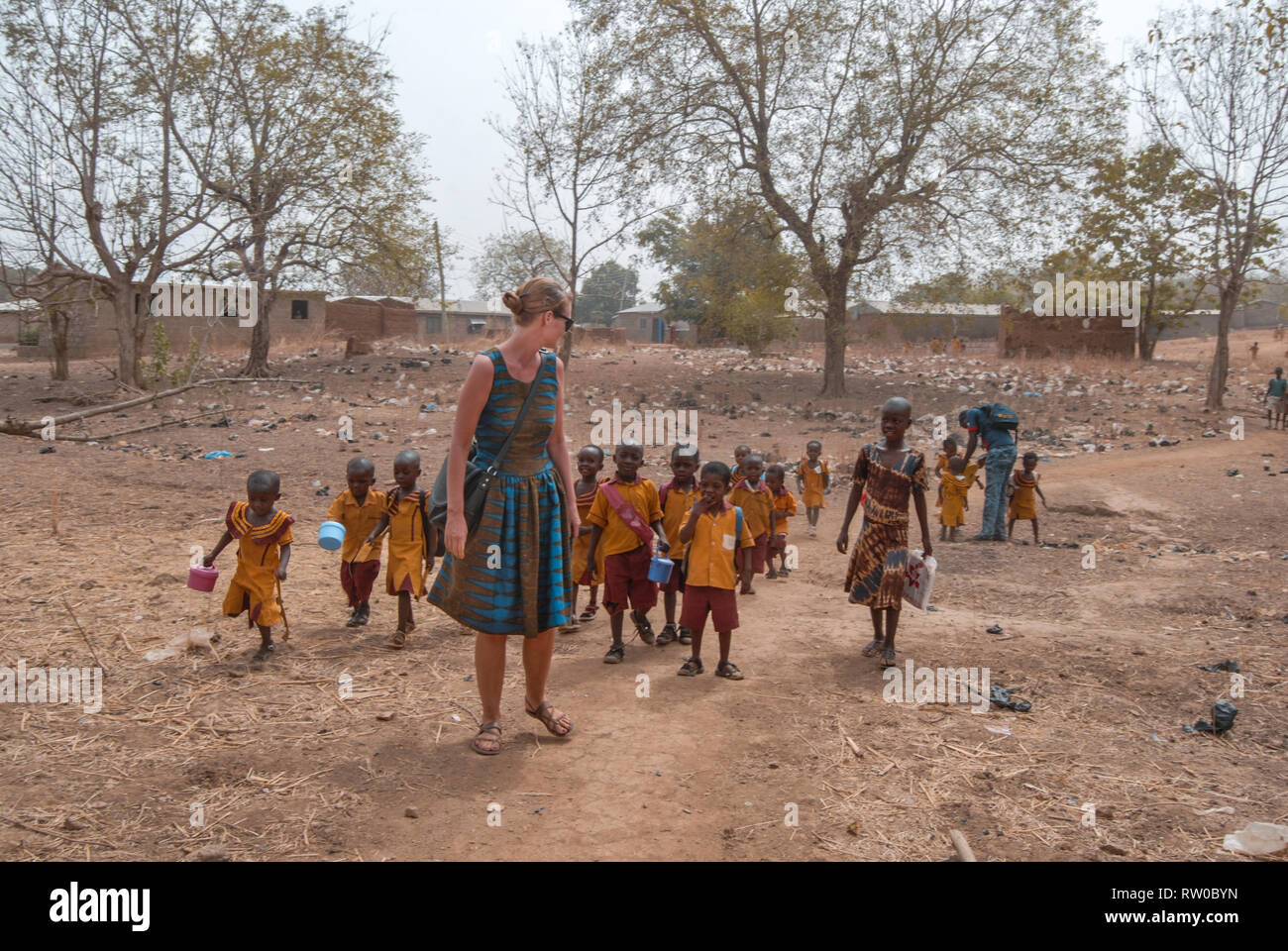 Une photo d'un travailleur social bénévole européen portant des vêtements traditionnels pour marcher avec les enfants des écoles ghanéennes Banque D'Images