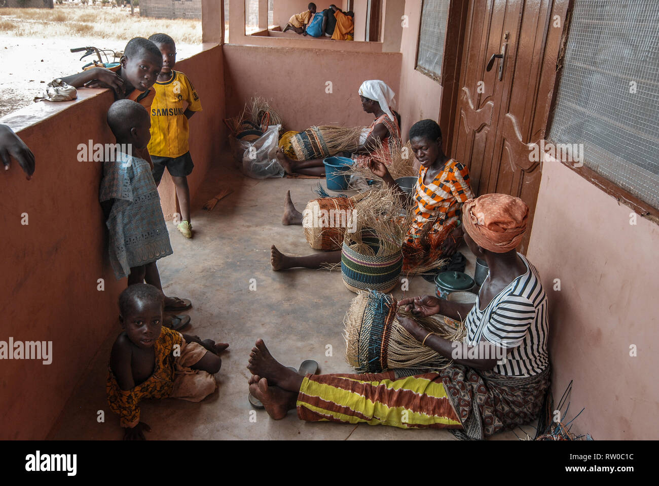 Une photo de femmes ghanéennes, assis sur un balcon et faisant de la célèbre Bolgatanga paniers du marché tandis que leurs enfants regardent et d'apprentissage Banque D'Images
