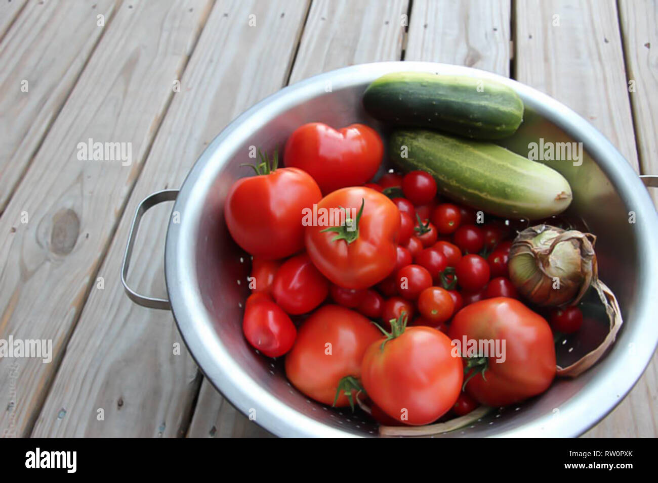 Bol en métal plein de tomates et concombres fraîchement cueillies sur terrasse en bois Banque D'Images