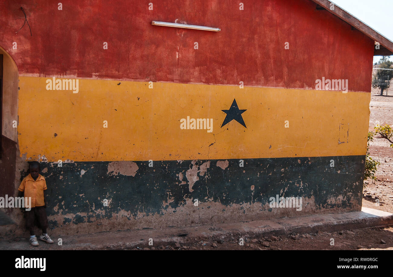 Un garçon posant sur l'arrière-plan d'une maison mur peint aux couleurs du drapeau du Ghana - rouge, jaune et vert. Banque D'Images