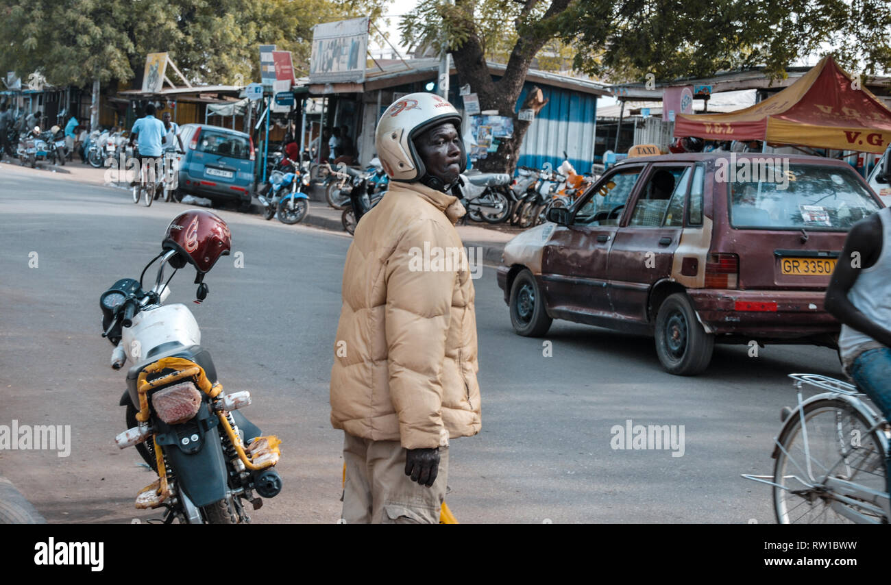 Une belle photo d'un pilote moto ghanéens portant un manteau d'hiver en marchant sur une rue de ville Bolgatanga Banque D'Images