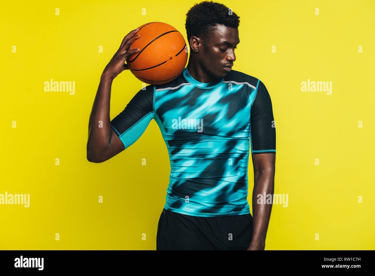 Homme africain avec le basket-ball sur son épaule. Joueur de basket-ball masculin contre fond jaune. Banque D'Images