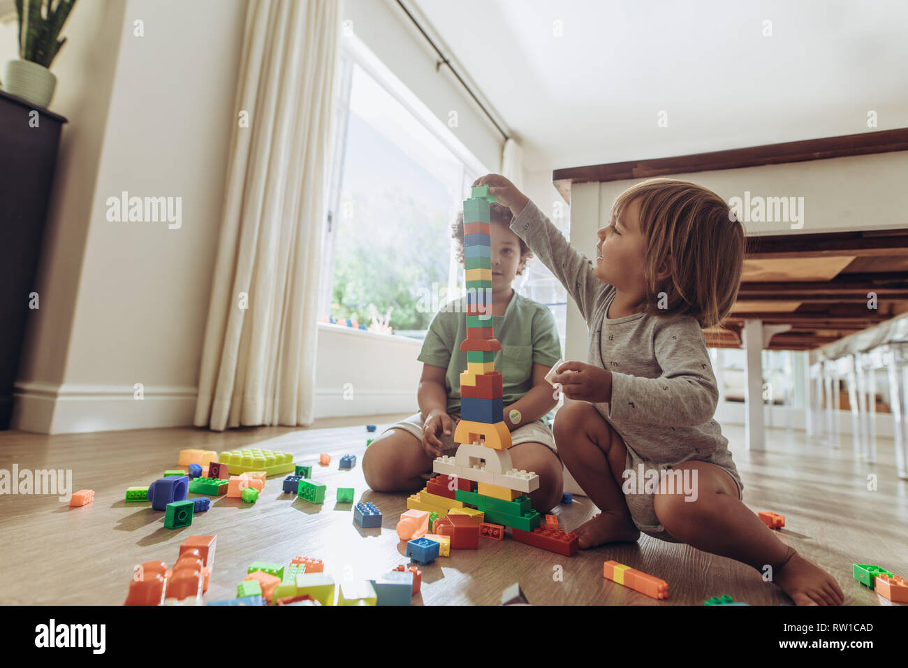 Kids une tour à l'aide de blocs de construction. Heureux les enfants jouant avec des jouets assis sur marbre à la maison. Banque D'Images