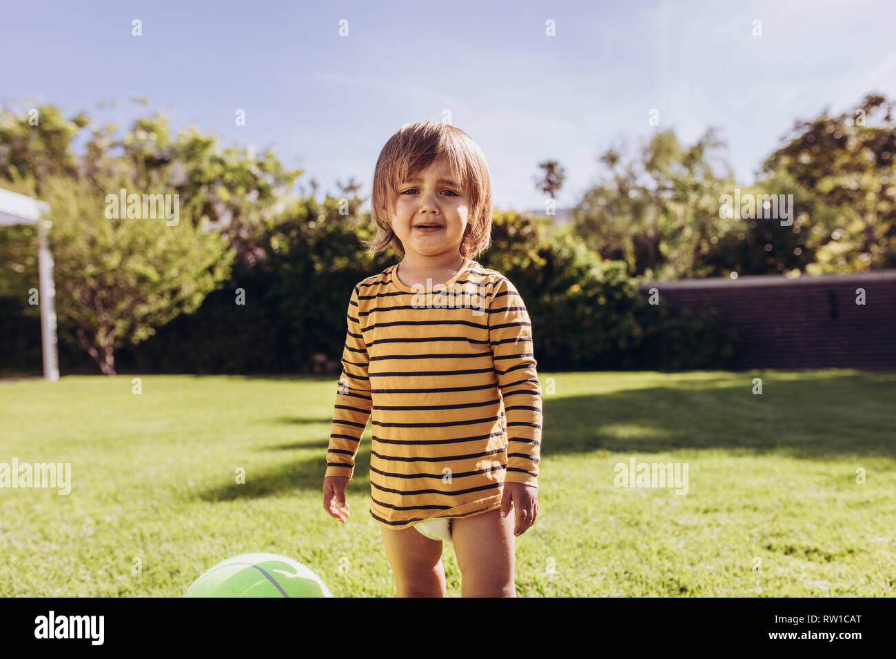 Portrait d'un garçon debout seul dans park et pleurer. Little boy playing with ball dans un parc sur une journée ensoleillée. Banque D'Images