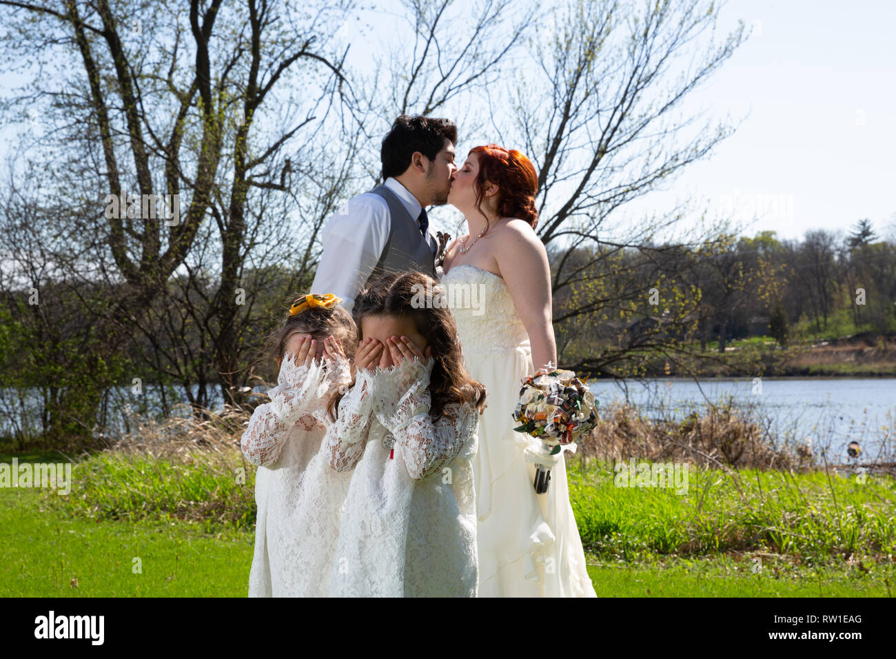 Bride and Groom kissing avec filles fleurs couvrant leurs yeux Banque D'Images