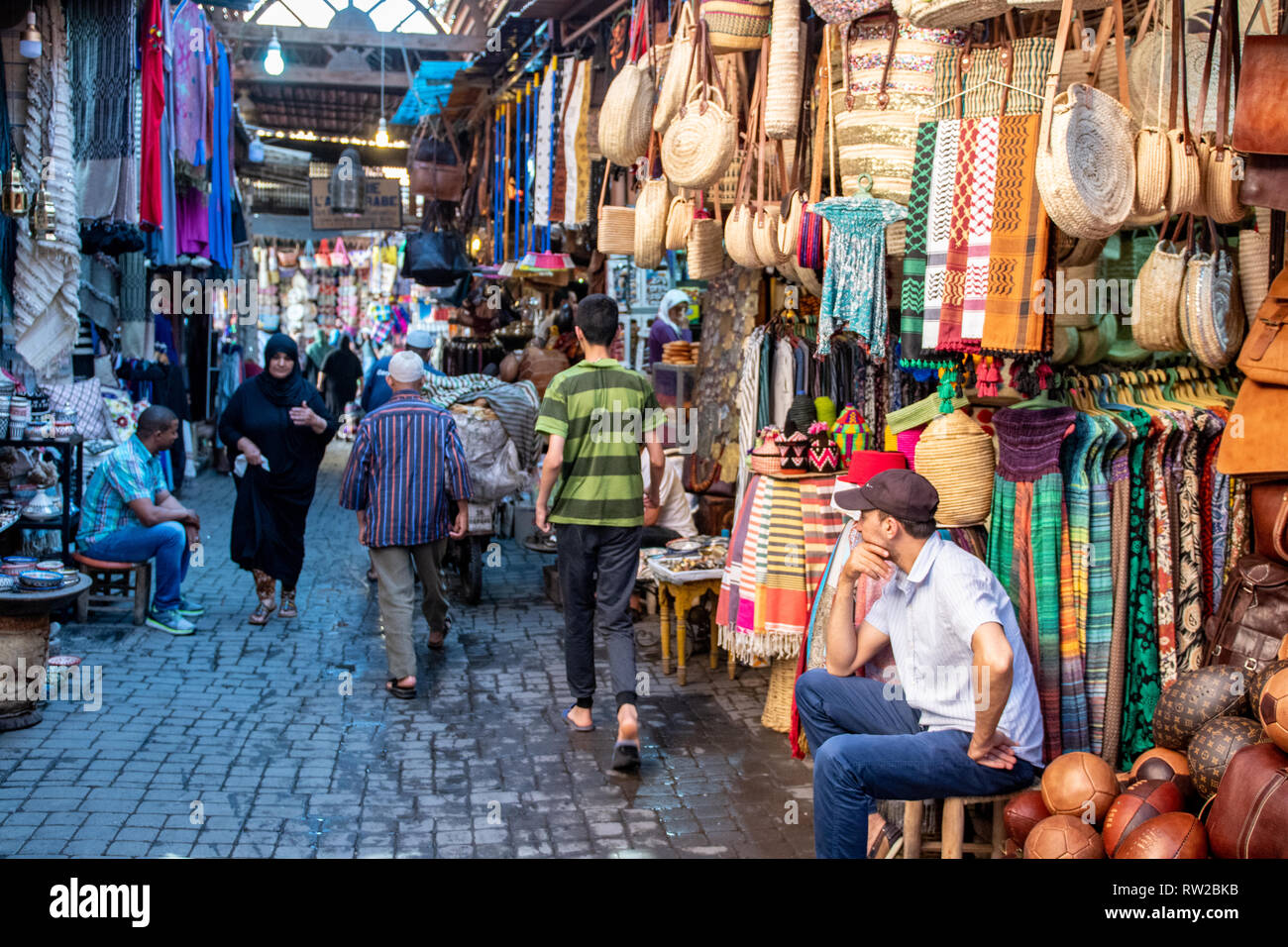 Les commerçants s'asseoir devant leur magasin comme avant-pied et les acheteurs naviguez sur ruelle de médina de Marrakech, Maroc Banque D'Images