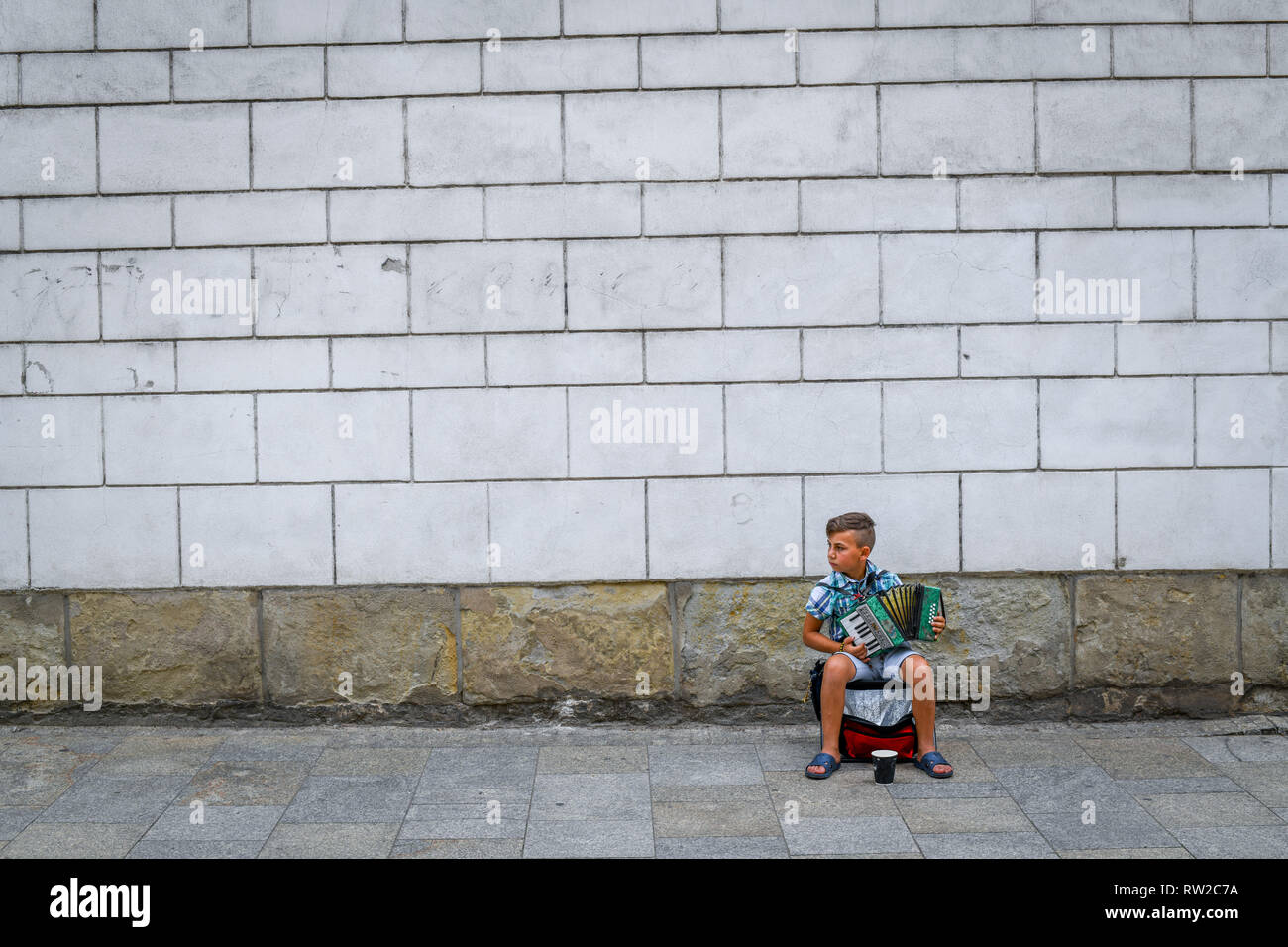 Le jeune enfant est assis et joue de l'accordéon musicien ambulant dans les rues de Krak-w, Lesser Poland Voivodeship, Pologne. Banque D'Images