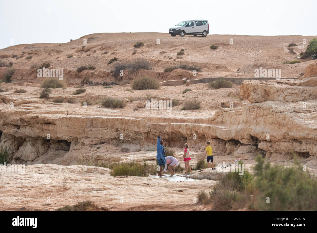 Les gens se rafraîchir dans un canal d'eau dans le paysage aride de l'Oasis de Tighmert, Maroc Banque D'Images