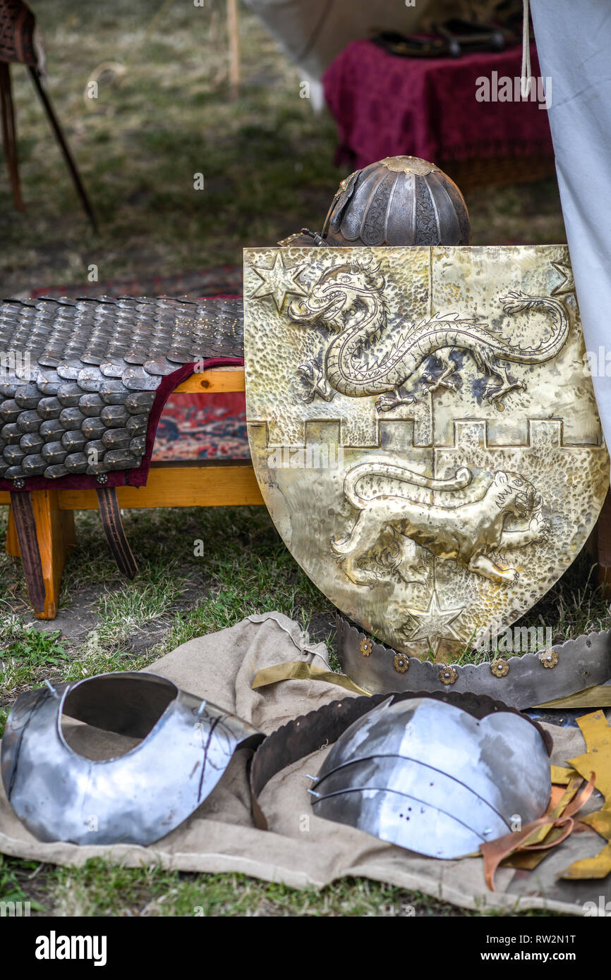 Un bouclier avec une représentation d'un dragon et grand chat sur ce qu'il repose contre un banc parmi une variété d'armures médiévales annuel à St John's Fair - Jarmar Banque D'Images