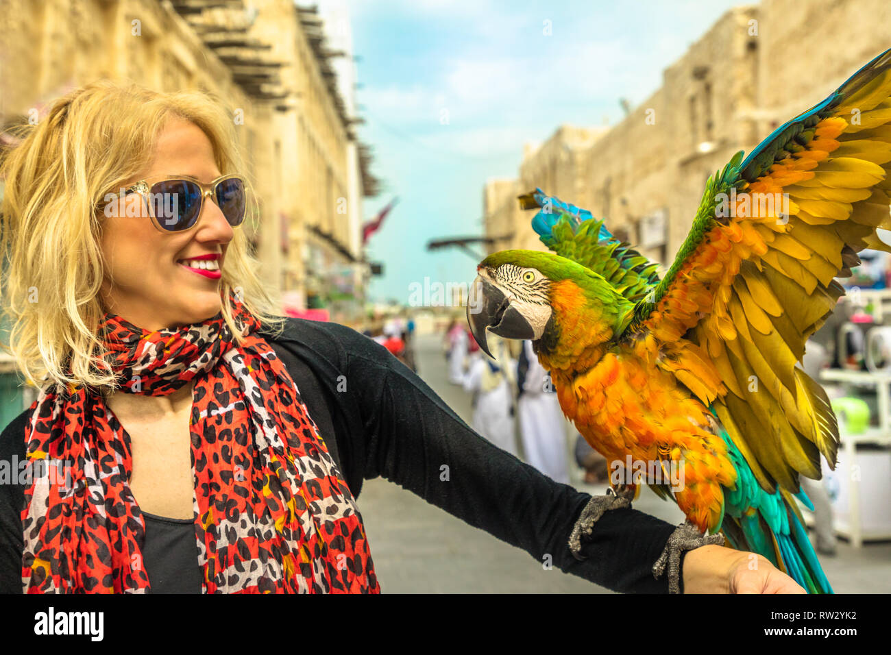 Portrait de femme interagit avec un perroquet avec ailes ouvertes au Souk d'oiseaux à l'intérieur de Souq Waqif, le vieux marché attraction touristique dans le centre de Doha, Qatar Banque D'Images