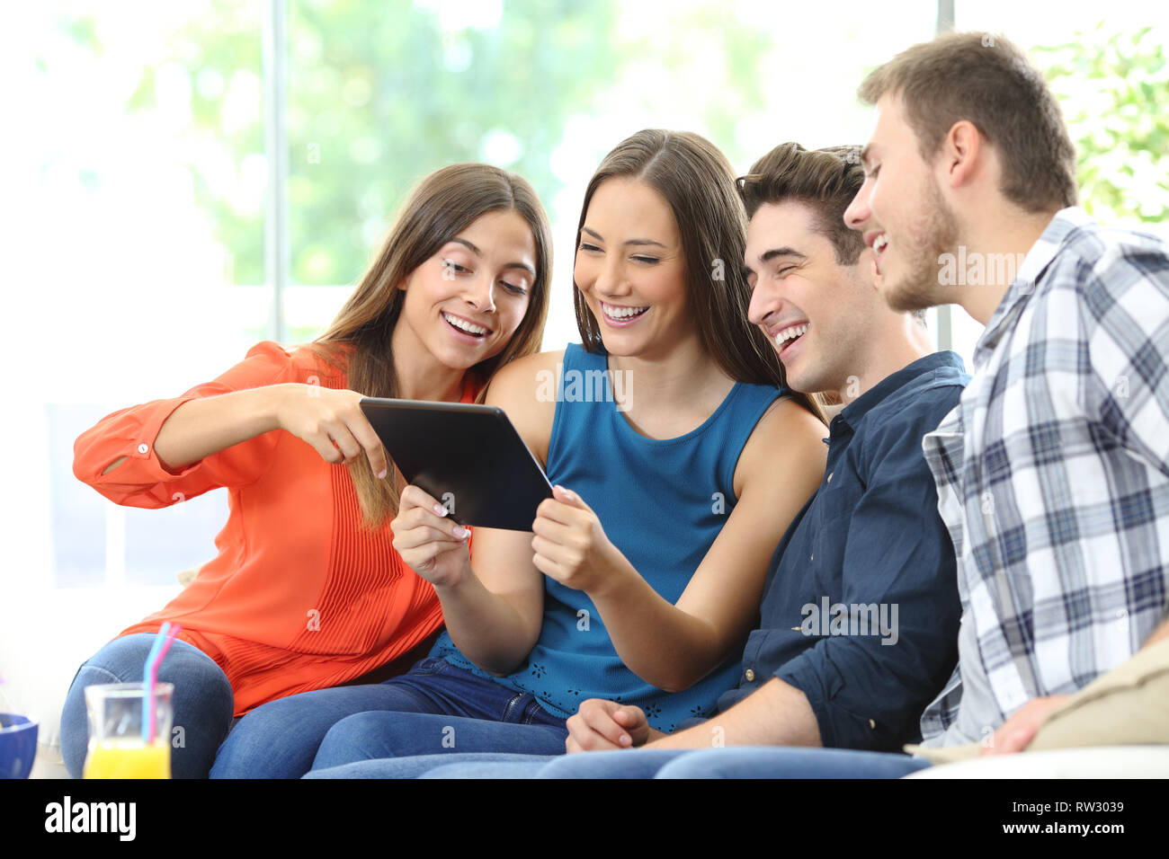 Groupe de quatre amis heureux contrôle contenu comprimé assise sur un sofa à la maison Banque D'Images