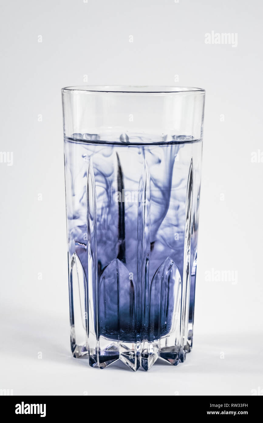 La pollution de l'eau concept. Substance foncée le mélange avec de l'eau propre dans un verre à fond blanc Banque D'Images