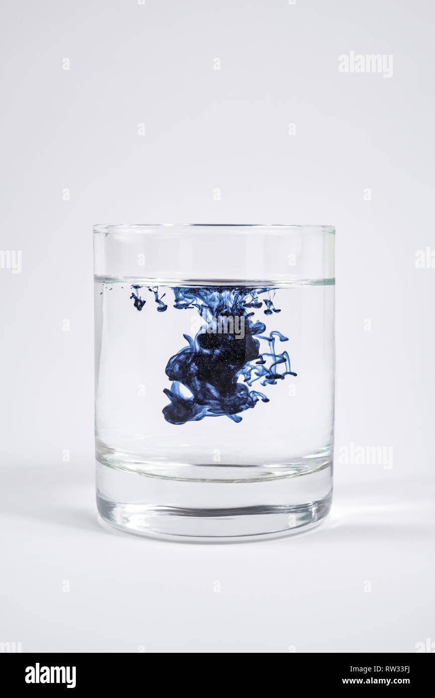 La contamination de l'eau concept. Substance foncée dissoudre avec de l'eau propre dans un verre à fond blanc Banque D'Images