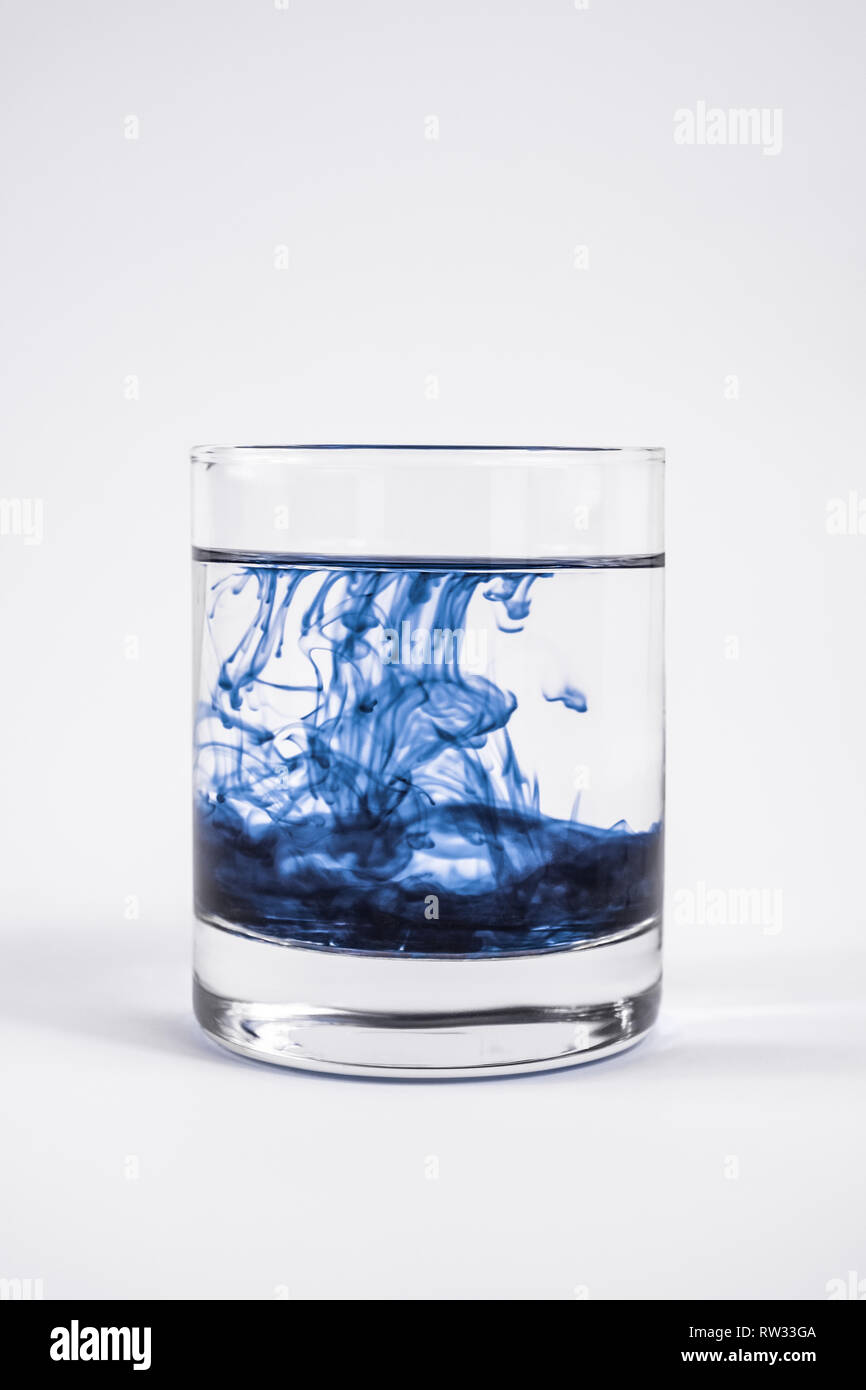 La contamination de l'eau concept. Substance foncée dissoudre avec de l'eau propre dans un verre à fond blanc Banque D'Images