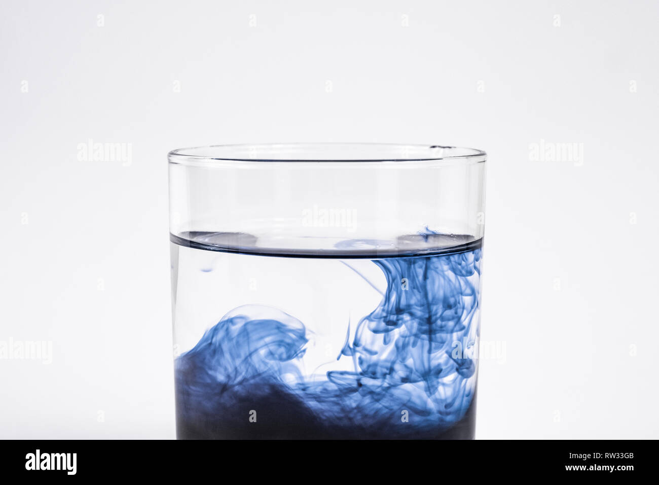 La contamination de l'eau concept. Substance foncée dissoudre avec de l'eau propre dans un verre à fond blanc, close-up view Banque D'Images