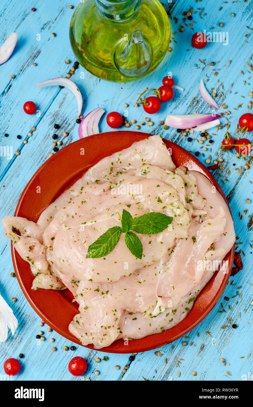 Portrait de quelques filets de poulet cru mariné dans une assiette en faïence marron, placé sur une table en bois rustique bleu à côté d'un verre cruet avec ol Banque D'Images