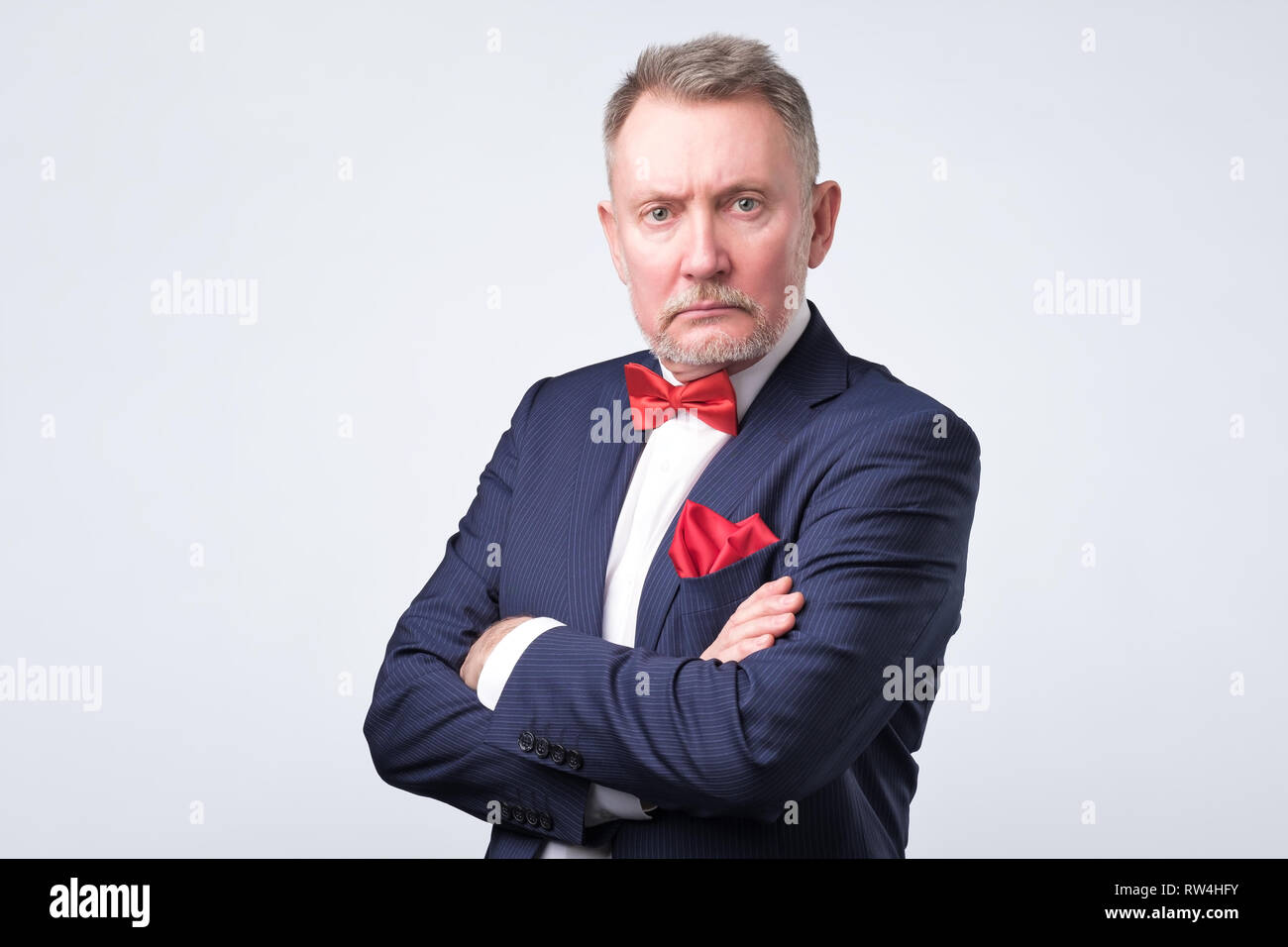 Senior businessman en costume bleu nous regarde sur fond gris. Banque D'Images