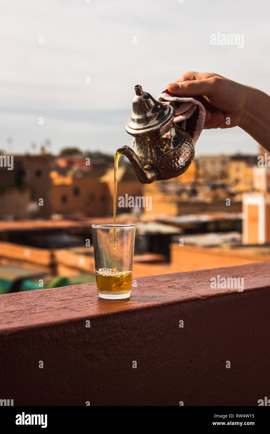 Verser le thé de menthe marocaine typique d'un karraffe d'argent dans un verre de thé au-dessus des toits de la médina de Marrakech (Marrakech, Maroc, Afrique) Banque D'Images