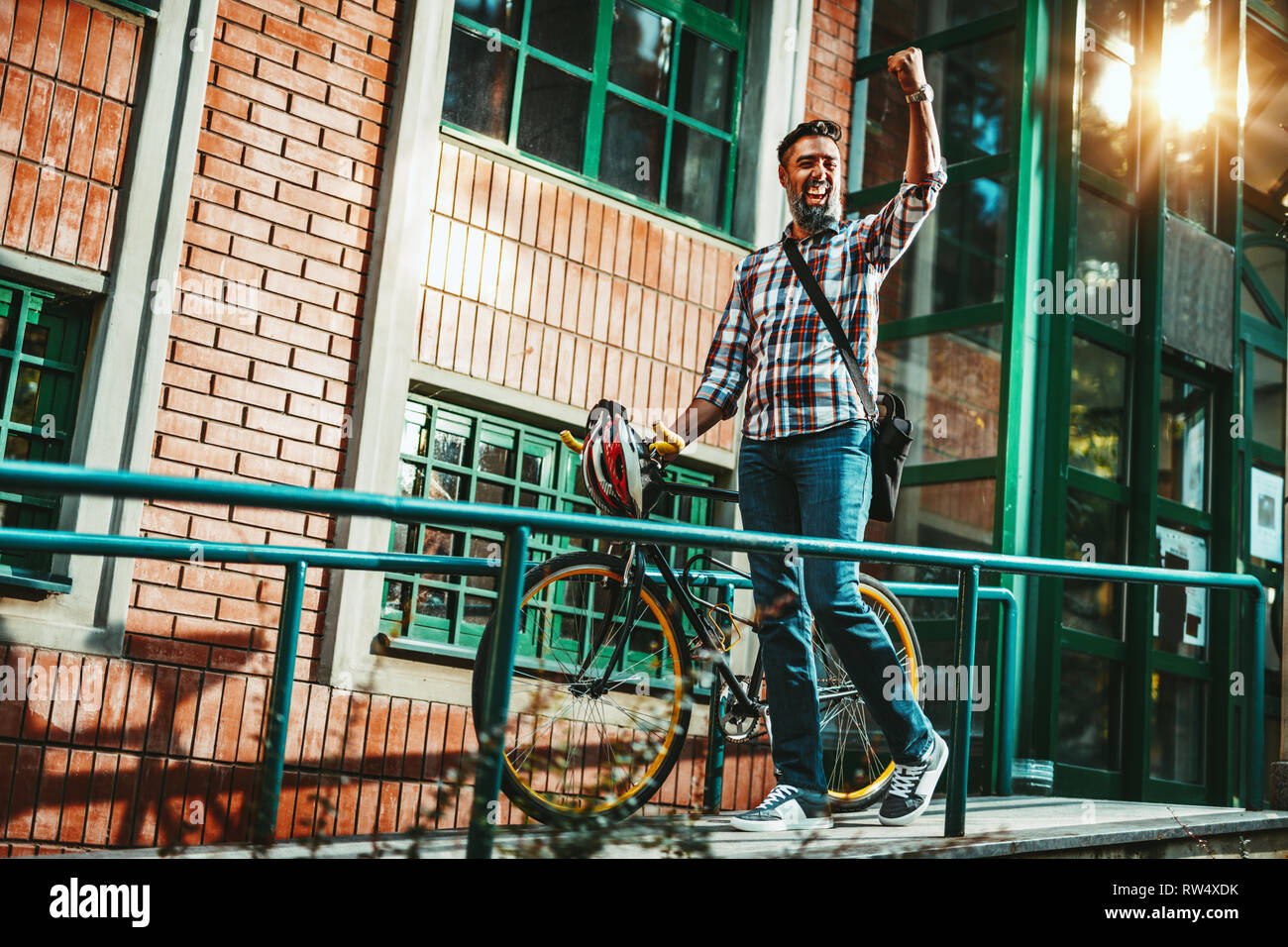 Un beau jeune homme va à la ville avec son vélo, debout à côté d'elle et célèbre son succès. Banque D'Images