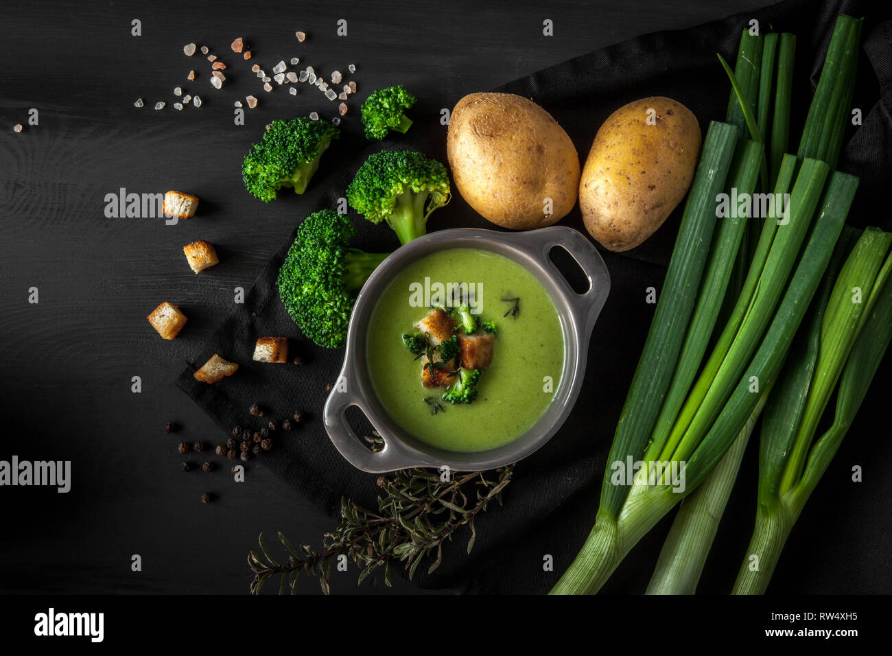 Detox de printemps vert soupe crème de brocoli avec pommes de terre et crème vegan dans un bol en bois sombre sur fond noir au conseil, vue du dessus. Manger propre Banque D'Images