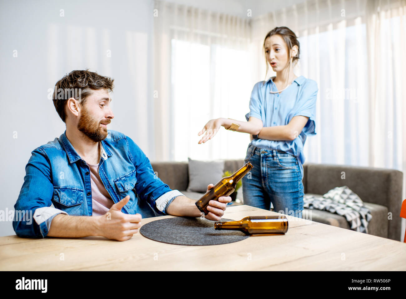 Ivre l'homme souffrant d'alcoolisme déprimé assis à la maison avec jeune femme dans le désespoir sur l'arrière-plan Banque D'Images