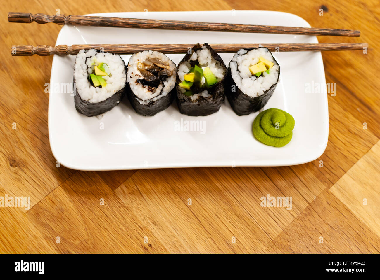 Vue de côté des rouleaux de sushi végétaliens rempli avec de l'avocat sur une petite plaque sur une table en bois avec de la sauce soja, wasabi et gingembre Banque D'Images