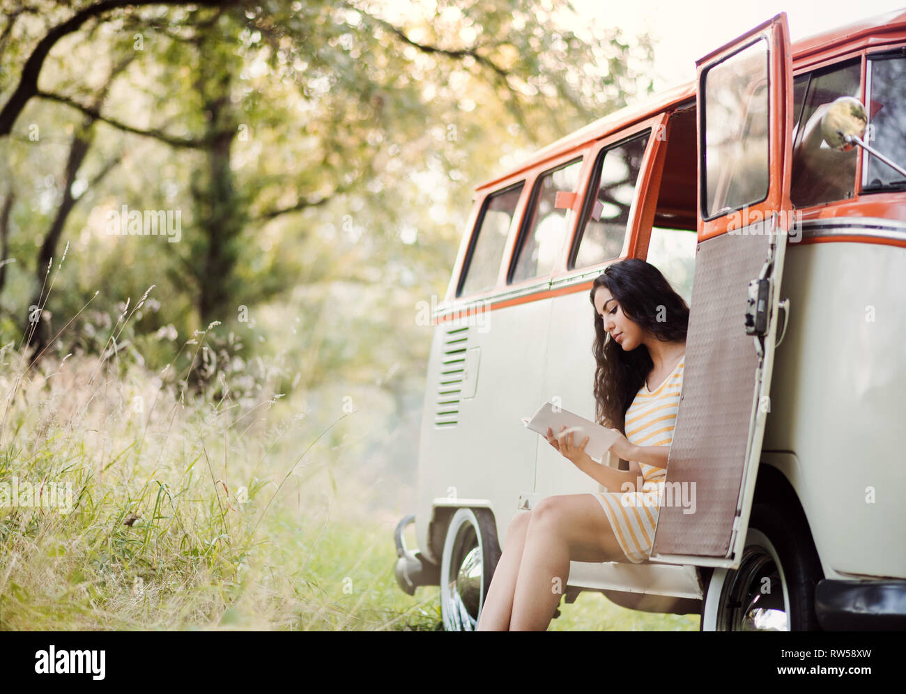 Une jeune fille avec un livre par une voiture sur un roadtrip à travers campagne, lecture. Banque D'Images