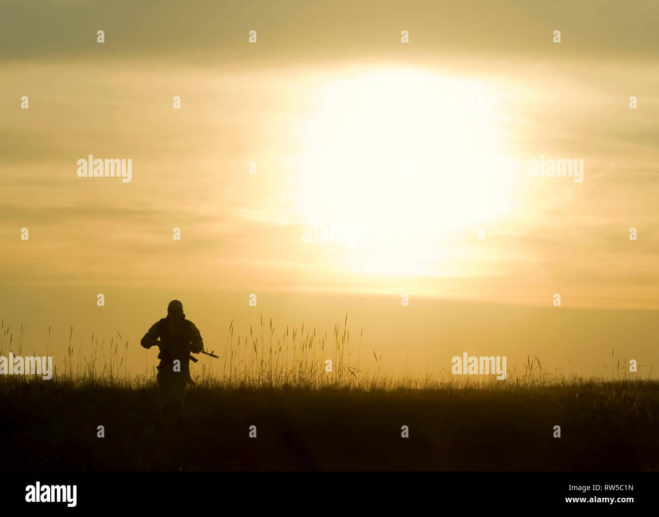 Silhouette de soldat au fusil contre un coucher de soleil. Banque D'Images