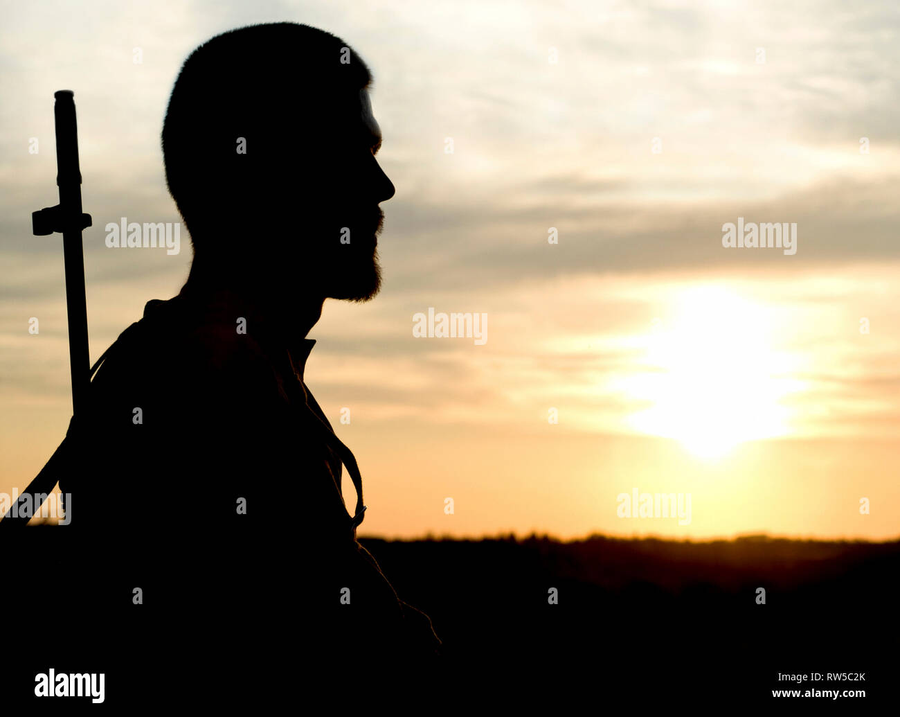 Silhouette de soldat au fusil contre un coucher de soleil. Banque D'Images