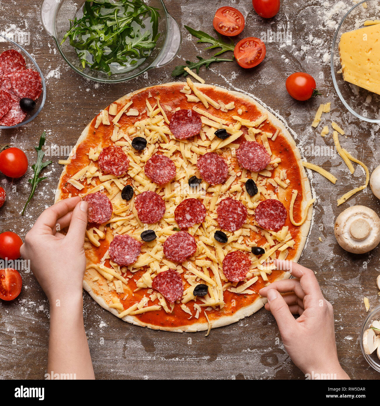 Woman putting on pizza salami, vue du dessus Banque D'Images